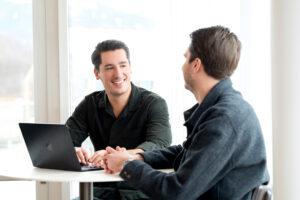 freundliche Geschäftsmänner im Gespräch bei Meeting, moderner Arbeitsplatz, erfolgreiche Zusammenarbeit, Business Meeting, Laptop, Teamarbeit