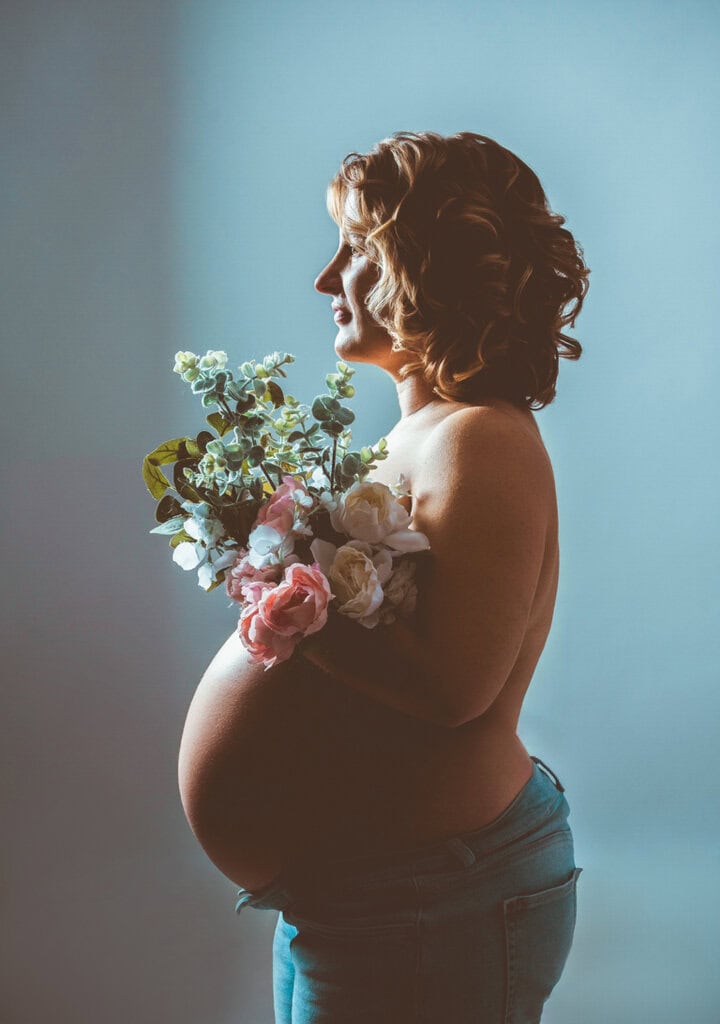 Natural pregnancy photography in Munich, beautiful woman with flowers and baby bump, professional photo shoot at Photogenika Photo Studio.