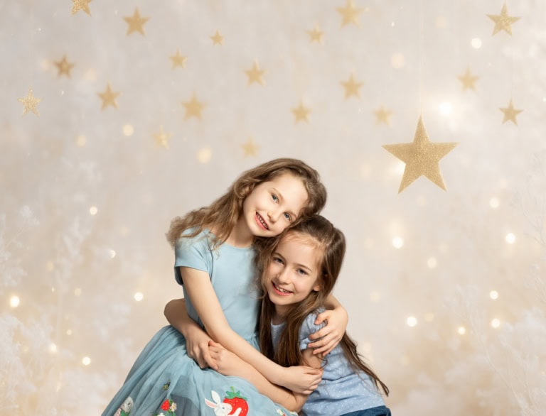 Zwei lachende kleine Mädchen umarmen sich vor einem Weihnachtsstern-Hintergrund, kreative Kinderfotografie für festliche Anlässe und Familienporträts in München.