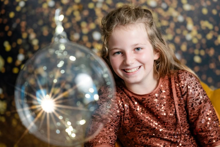 Lächelndes Mädchen in Goldsternen-Backdrop mit Ballon, professionelles People-Foto in München, Panoramaaufnahme.