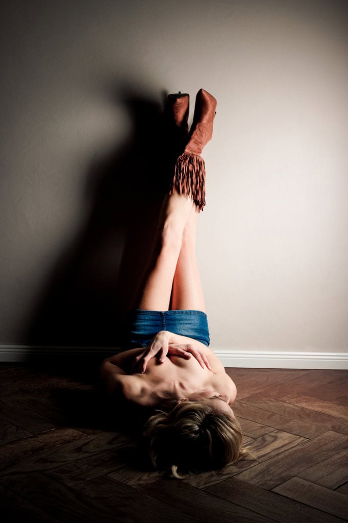 Creative artistic nude photography of a woman lying on the floor with her legs against the wall, with shadows and subtle lighting, shot in a professional photo studio in Munich.