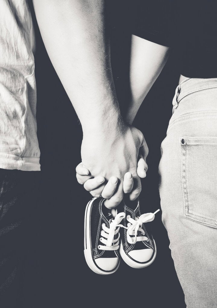 Black and white photo of a couple posing in Munich at Photogenika Photo Studio, wearing children's sneakers, depicting love and togetherness, ideal motifs for family and couple photography.