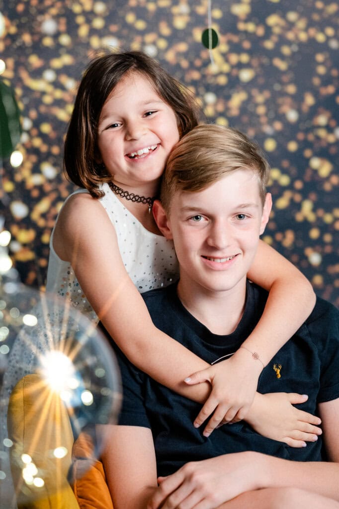 2. Hochwertiges Porträtfoto zweier Kinder bei einer Studioaufnahme in München, lachend und umarmend, mit bokeh artigem Hintergrund und warmem Licht, Highlight für Familienfotografie.