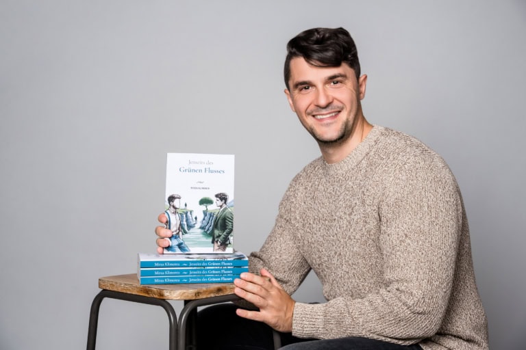 Professional portrait of a man presenting a book against a neutral background.