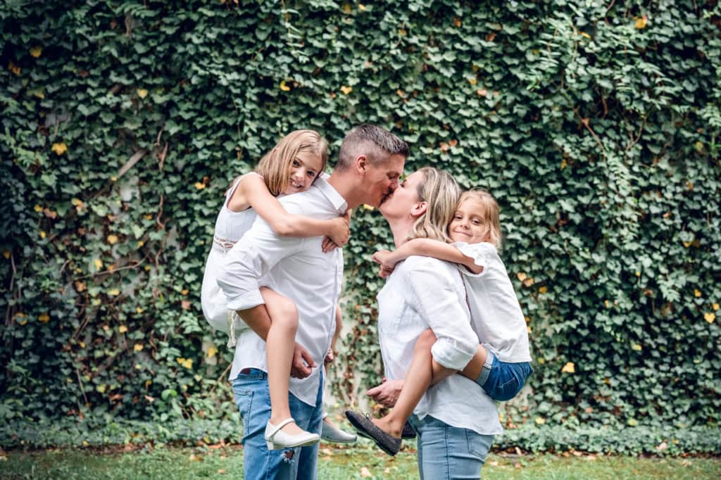 Fröhliche Familie beim Kuss im Grünen, hochwertige Familienfotografie in München, professionell, emotional und natürlich für unvergessliche Familienmomente.