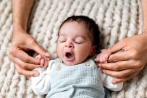 Neugeborenes gähnt herzhaft in blauer Latzhose gehalten von Händen