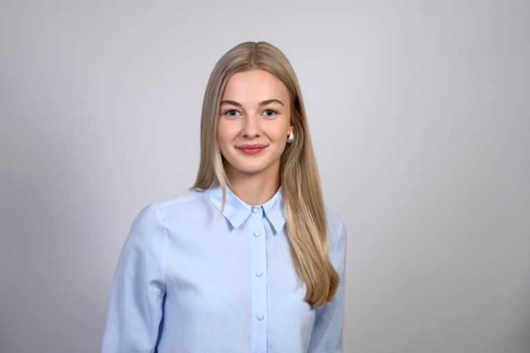 A young woman with blonde hair and a blue blouse smiles kindly.