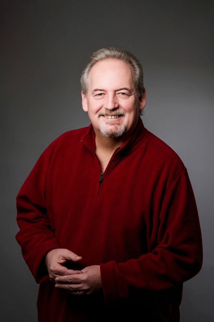 Portrait of a man with a beard and a red fleece pullover against a grey background.