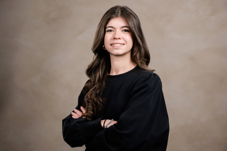 Woman with long dark waves and a black top crosses her arms.