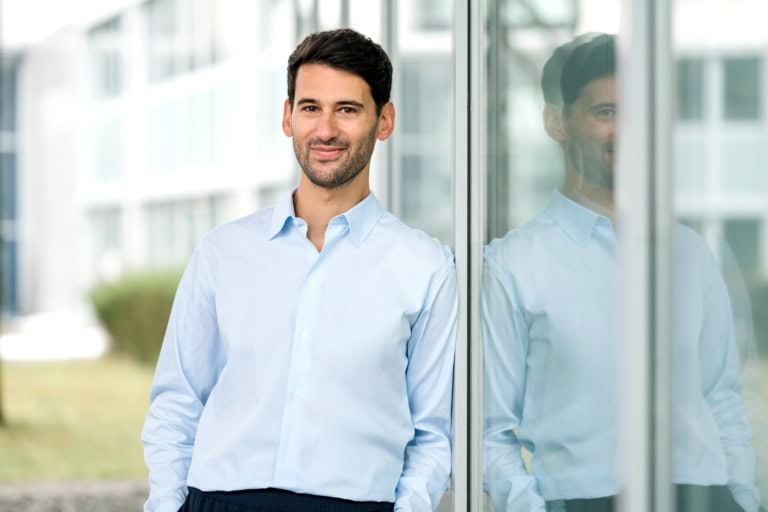Business portrait of a man in a blue shirt leaning against a window.