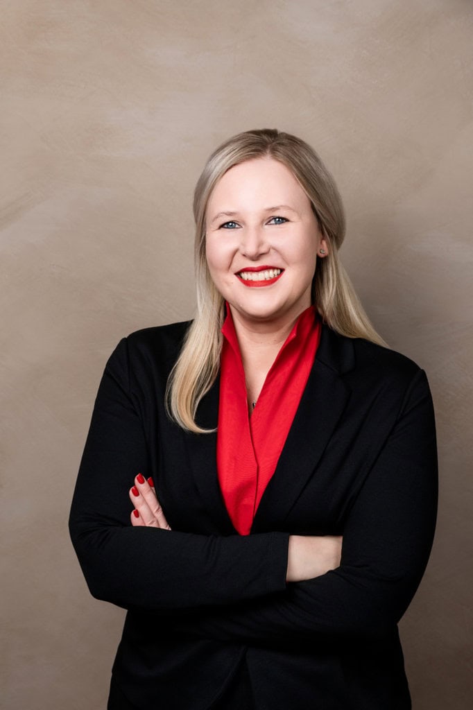 Attractive business portrait of a professional woman in a black blazer with a red scarf, posing with arms crossed in front of a neutral background, ideal template for business and application photos.