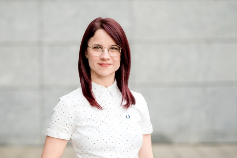 1. Young woman with red hair and glasses in front of a grey wall background, professional portrait, high-quality photography.