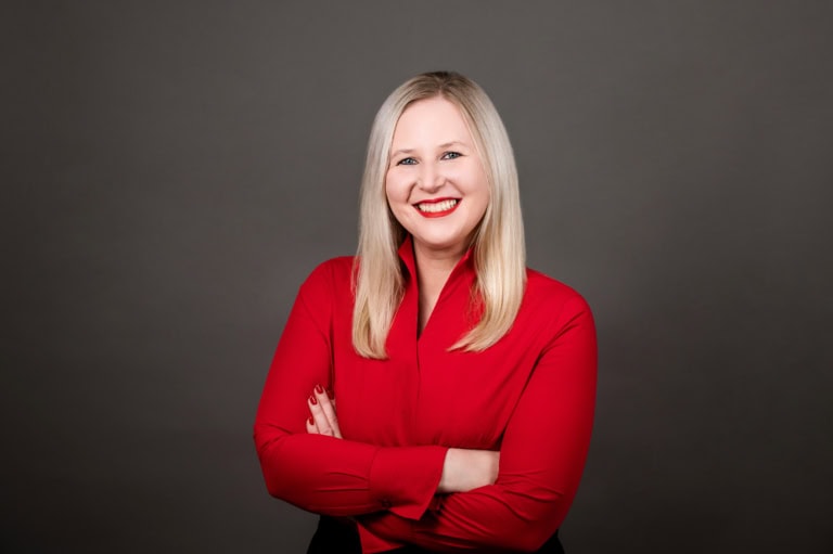 Portrait of a smiling woman in a red blouse against a dark background.