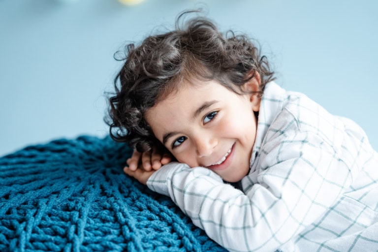 Ein Junge mit Locken liegt entspannt auf einem blauen Kissen.