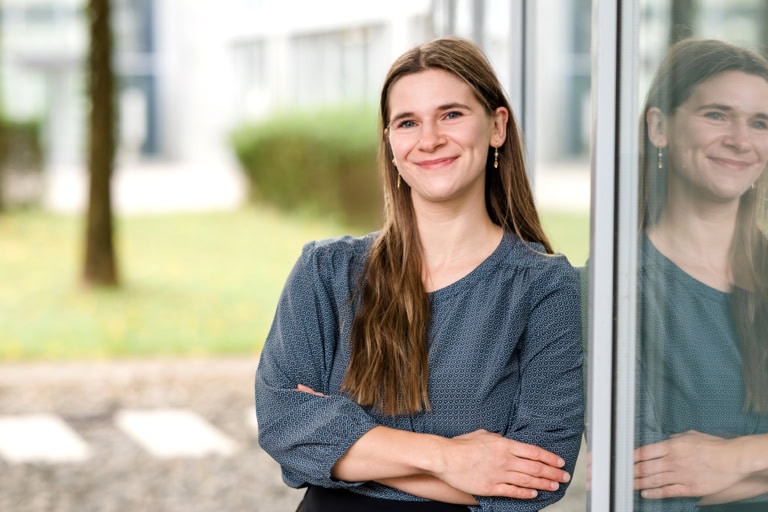 Natural portrait of a woman with long hair leaning against a window.
