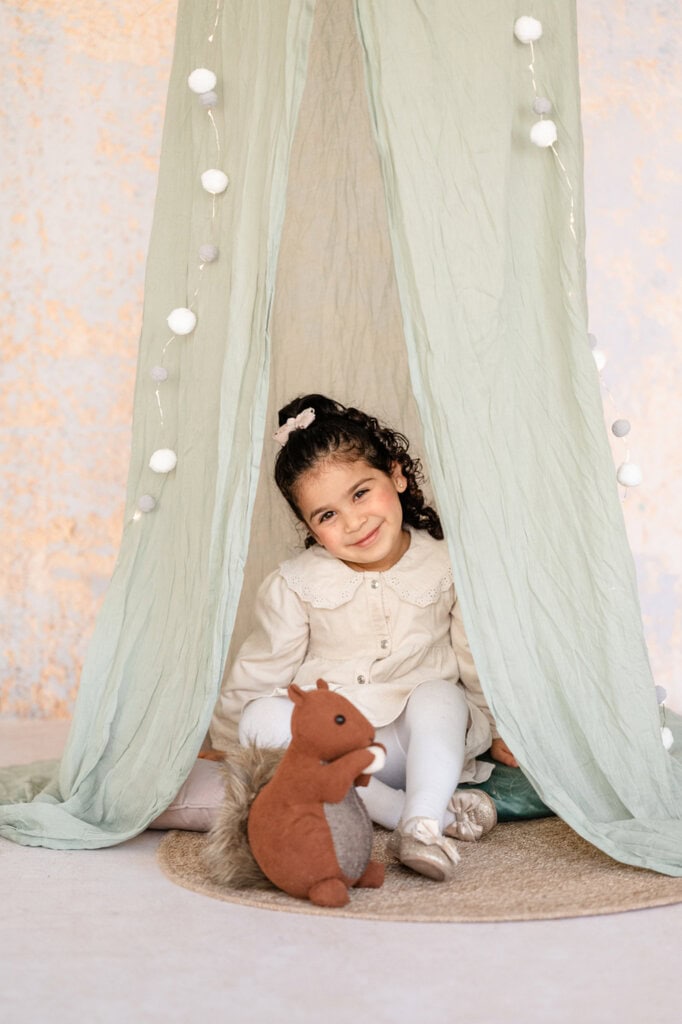 Ein Mädchen sitzt mit einem Stoff-Eichhörnchen im Spielzelt.