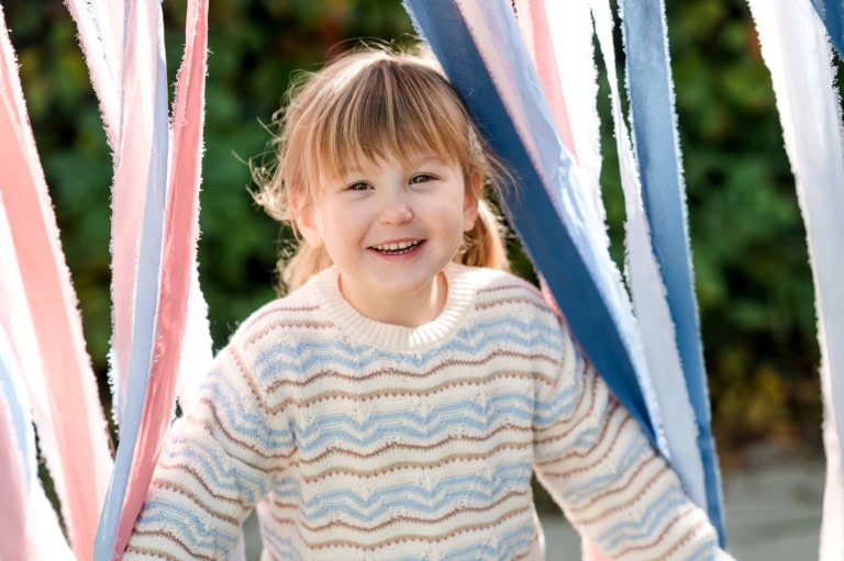 Ein fröhliches Kind schaut durch bunte Stoffbänder hindurch.