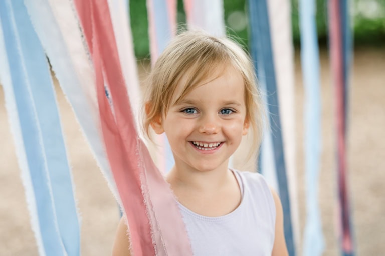 Ein strahlendes Mädchen steht vor einem Vorhang aus bunten Bändern.