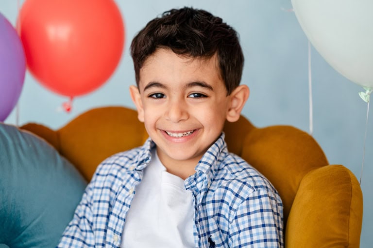 Ein Junge im karierten Hemd sitzt in einem Sessel umgeben von Ballons.