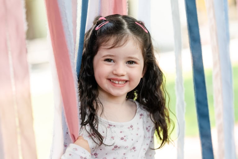 Ein Kind schaut neugierig durch herabhängende Stoffbänder.