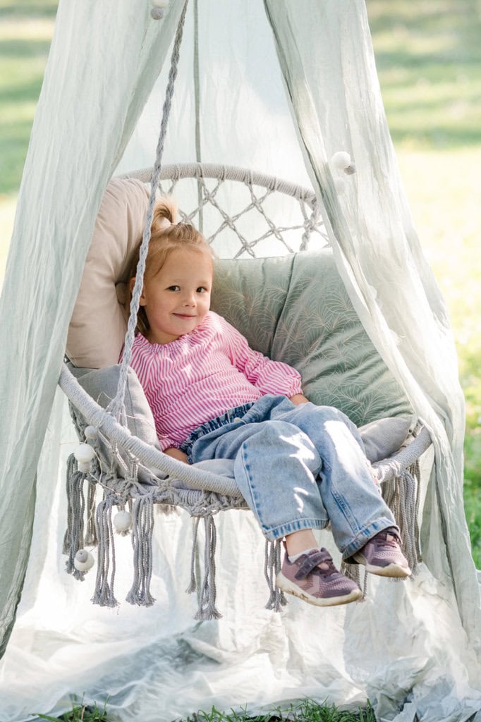 Ein Kind entspannt sich in einer Makramee-Schaukel im Garten.