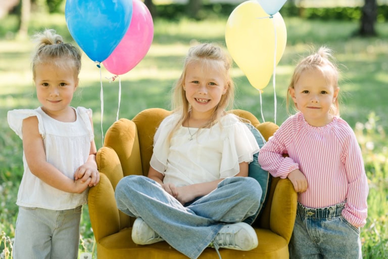 Drei Mädchen posieren fröhlich um einen gelben Sessel mit Ballons.