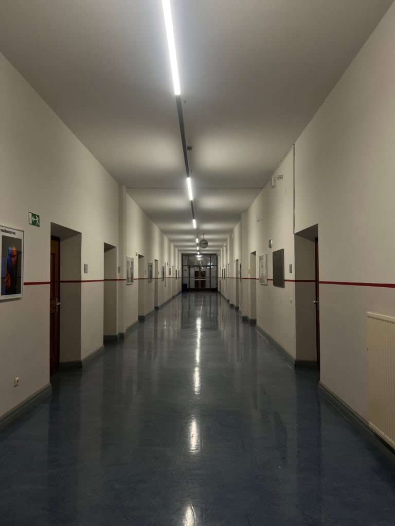 Empty hallway in a school building, modern lighting, bright walls, newspaper or poster frames, calm ambience, clean lines, reflective floors, tranquil atmosphere, professionally photographed.