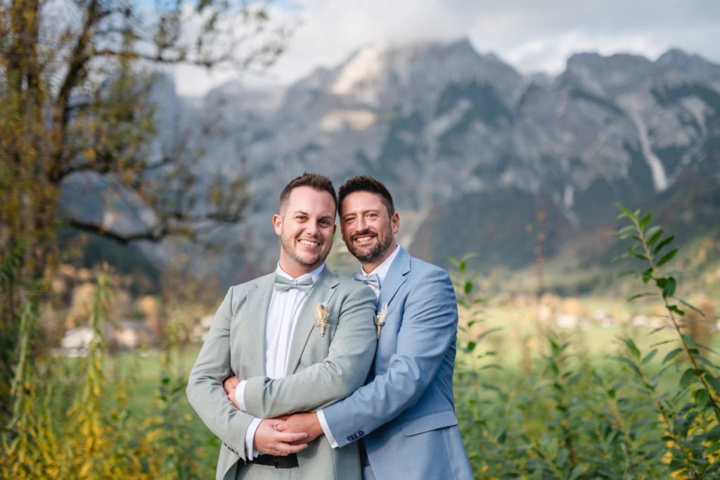 Glückliches Männerpaar umarmt sich vor beeindruckender Bergkulisse.