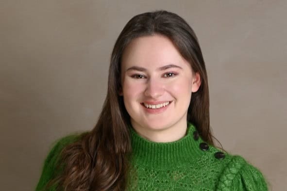 Smiling young woman with brown hair in a green sweater against a neutral background.