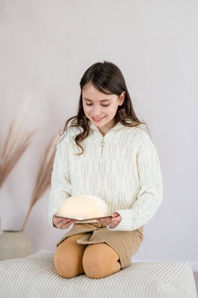 Mädchen kniet und hält eine leuchtende Buchlampe