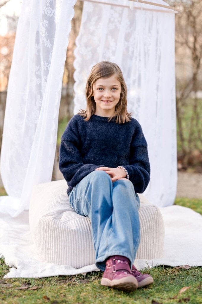 Mädchen im dunkelblauen Pullover sitzt draußen auf einem Sitzsack